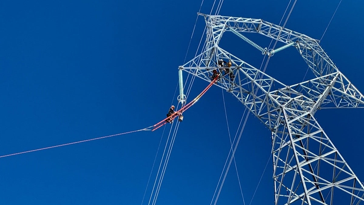 Lineman working on a high-voltage transmission tower with a Barry insulating rope